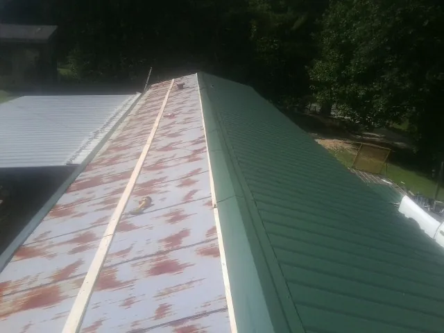 Old rusted panels beside newly installed green metal roofing — Wind Damage Roof Repair by Roofing Brothers in Cambridge