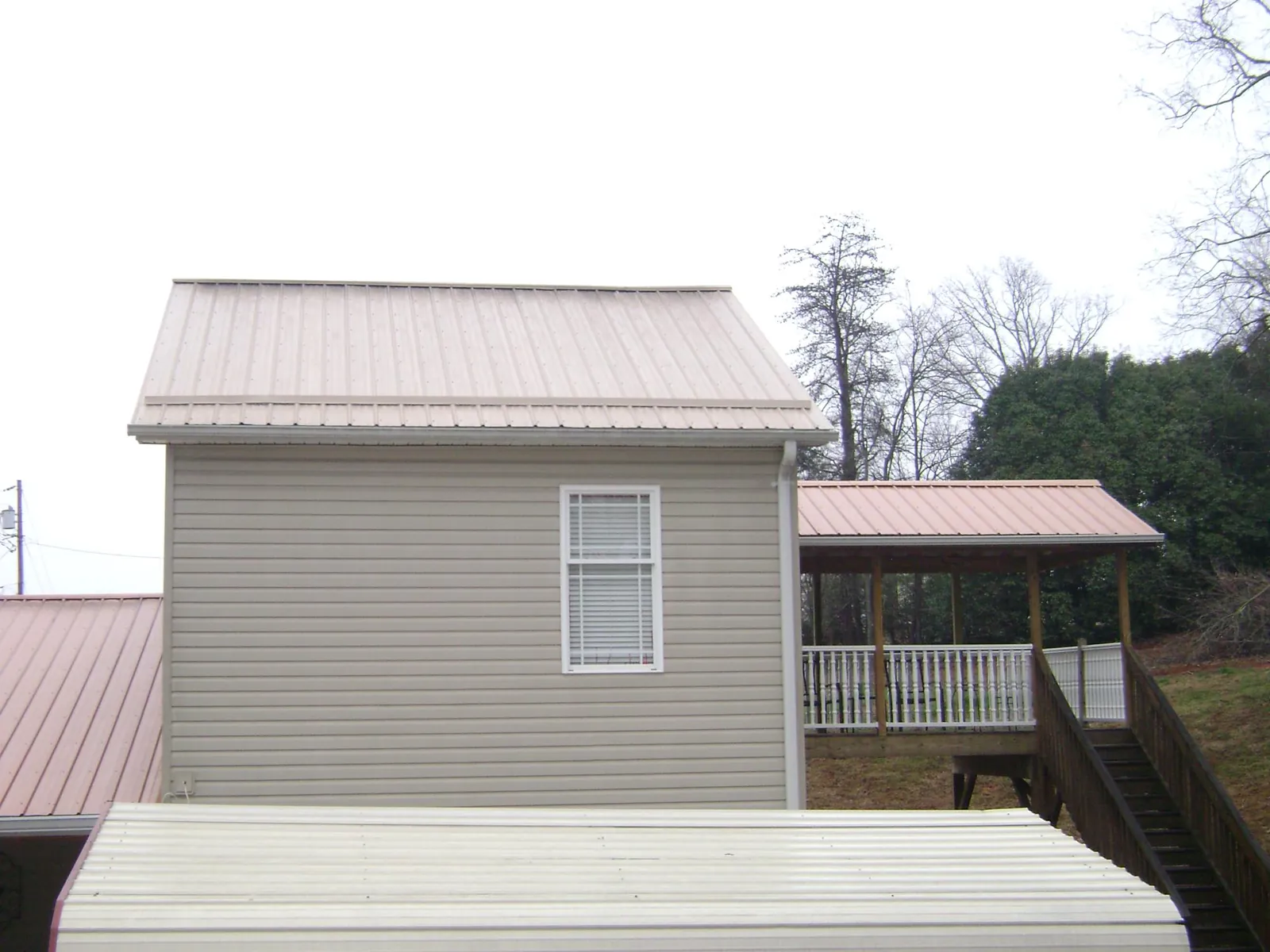 Tan metal roofs on a two story addition and attached porch, from a Roof Replacement job in Cambridge